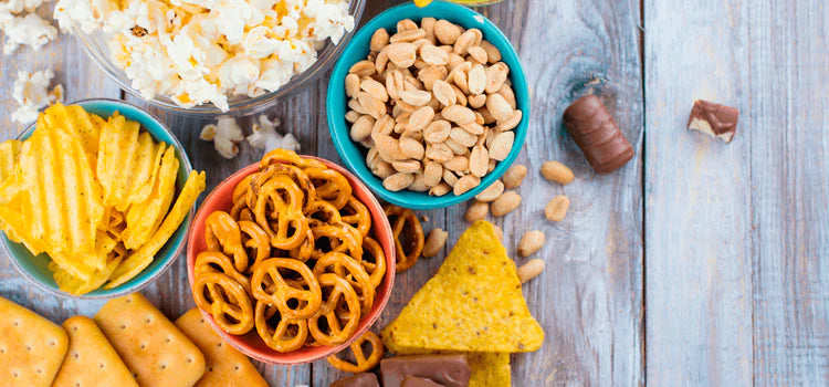 Snacks wie Popcorn, Brezeln, Nüsse und Chips in bunten Schalen