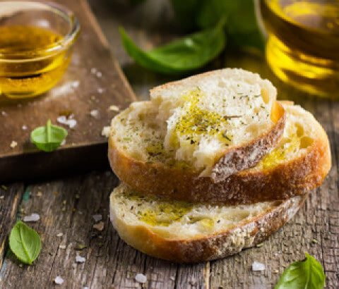 Frisches Brot mit Olivenöl, Meersalz und Kräutern auf rustikalem Holztisch – mediterrane Vorspeise mit Basilikum.